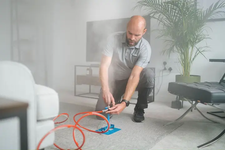 A technician setting up dry fog equipment in a living room